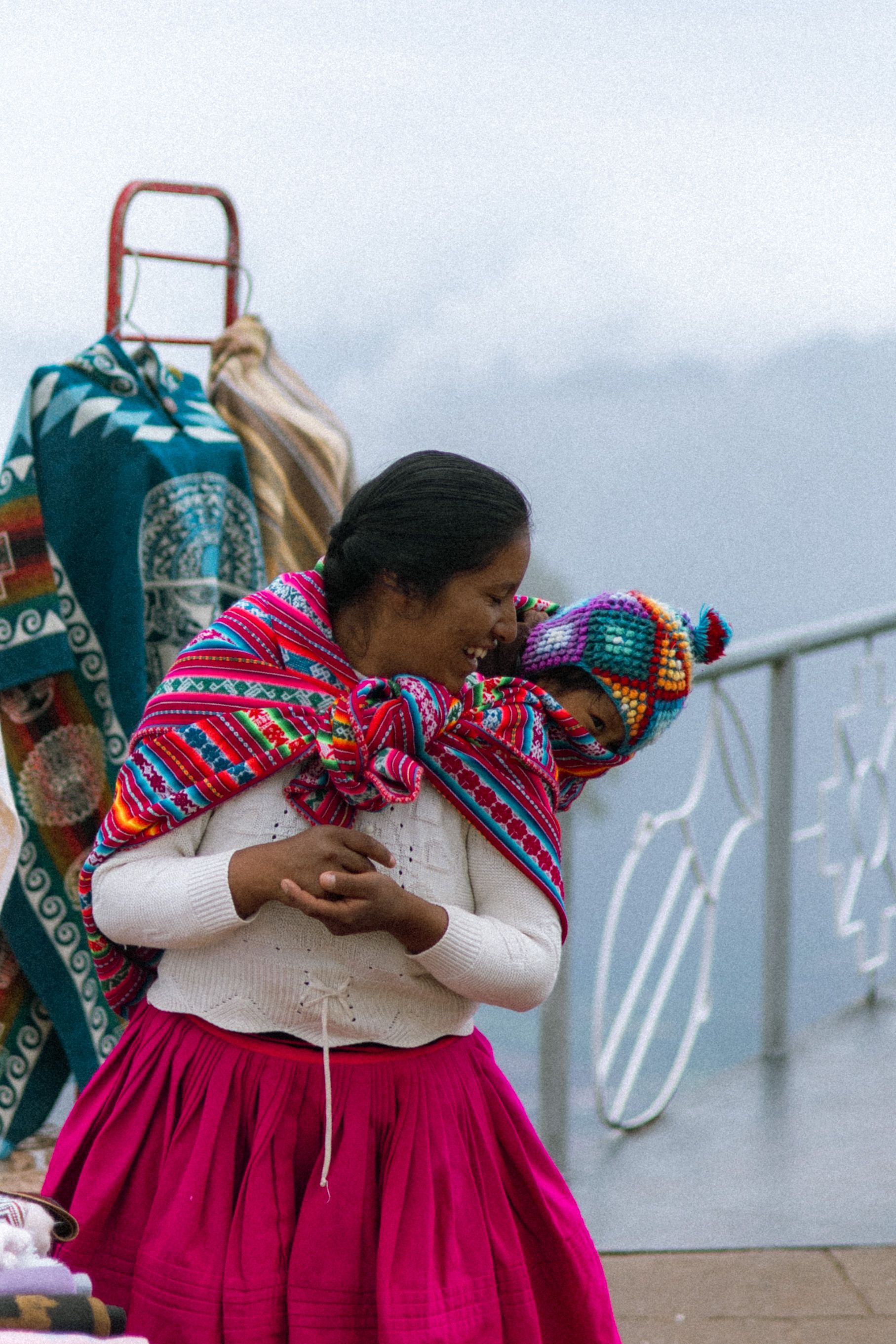 A mother in traditional Andean dress carrying her baby wrapped in a colorful textile in the Andes, South America